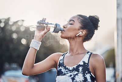 Buy stock photo One fit young mixed race woman taking a rest break to drink water from a bottle while exercising outdoors. Female athlete quenching thirst and cooling down after running and training workout in the city