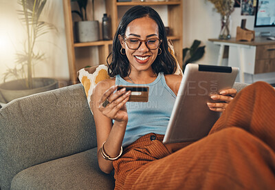 Smiling mixed race woman using credit card for ecommerce on digital tablet at home. Happy hispanic sitting alone on living room sofa, using technology for ebanking. Relaxing, ordering, buying online