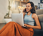 Beautiful mixed race woman using blogging laptop and cellphone to talk to clients in home living room. Hispanic entrepreneur sitting alone on floor and multitasking while networking on technology