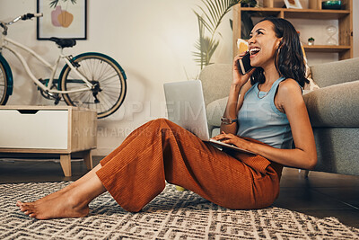 Beautiful mixed race woman using blogging laptop and cellphone to talk to clients in home living room. Hispanic entrepreneur sitting cross legged alone on lounge floor and networking on technology