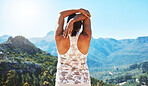 Rear view of a woman stretching her hand behind her head while standing outdoors. Woman exercising while overlooking a scenic mountain view. Living healthy active lifestyle