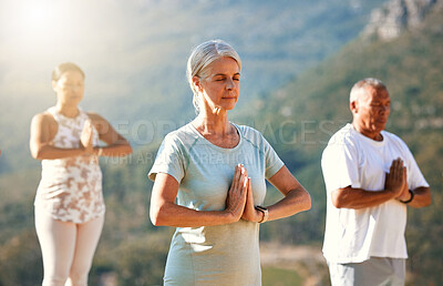 Three senior people meditating with joined hands and closed eyes breathing deeply. Multiethnic class of mature people doing yoga together in nature on a sunny day