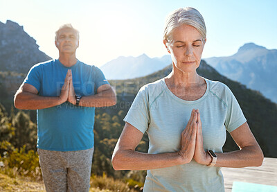 Senior couple meditating with joined hands and closed eyes breathing deeply. Mature couple doing yoga in nature living a healthy and active lifestyle in retirement