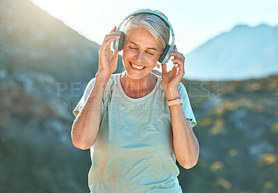 Buy stock photo Active senior woman wearing headphones and listening to music with her eyes closed. Mature woman standing outdoors against mountain background