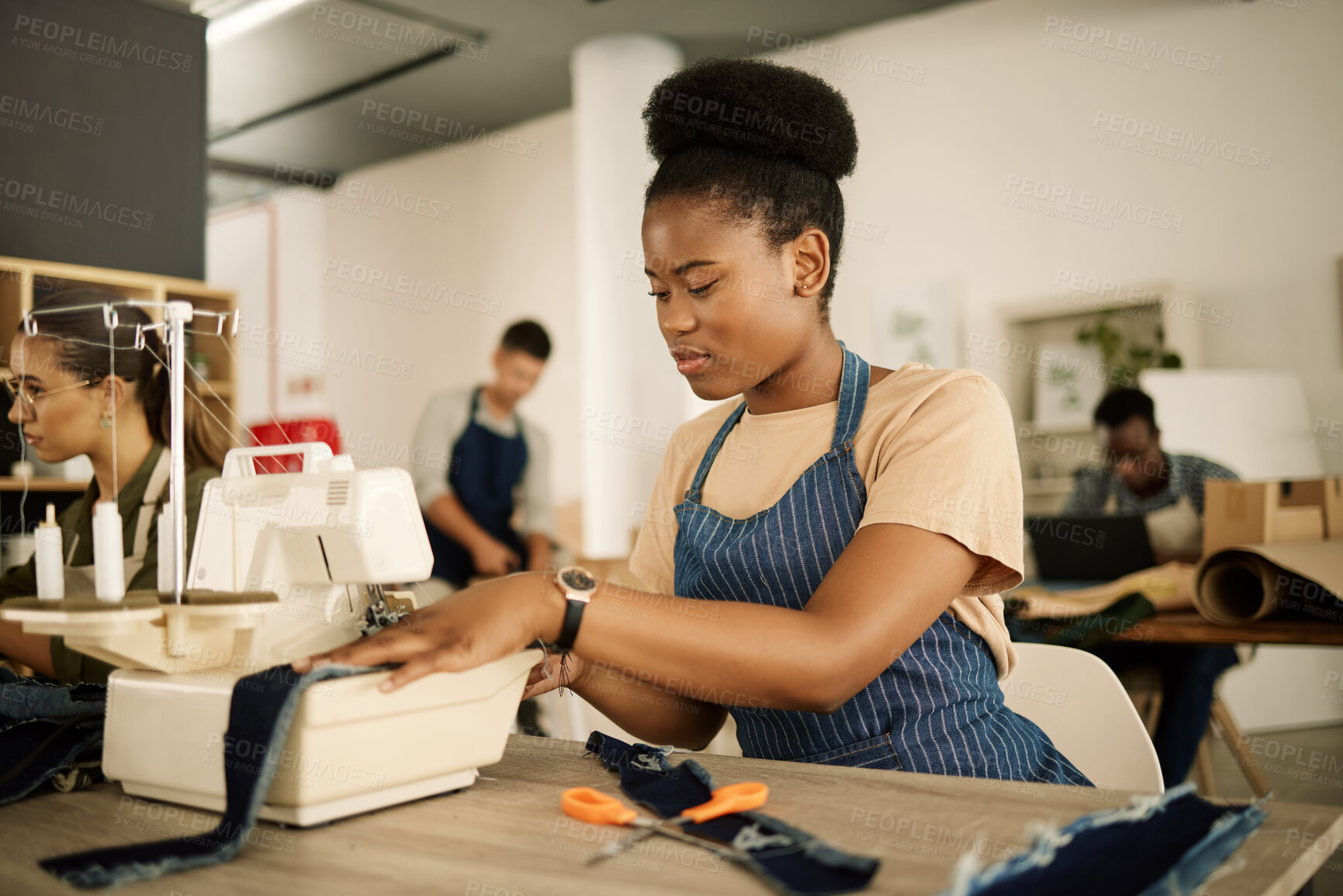 Buy stock photo Young designer sewing on a machine. African American tailor stitching a piece of denim. Fashion designer working at her table. Seamstress sewing material in her design studio.