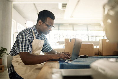 Buy stock photo Young businessman working on his laptop. African American tailor sending an email. Professional designer working online using his computer. Focused fashion designer using his laptop in the workshop