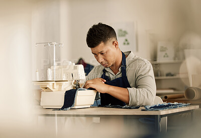 Focused tailor sewing on a machine. Young fashion designer stitching a piece of denim. Mixed race tailor using a sewing machine. Creative businessman working in his design workshop