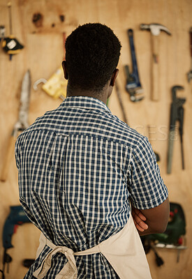 Buy stock photo Back of african american carpenter choosing his tools. Designer standing by a wall of tools and equipment. Creative entrepreneur deciding on tools to use. Businessman choosing equipment.