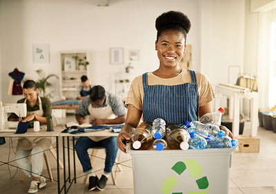 Smiling designer recycling plastic bottles. Young fashion designer holding recyclable plastic bottles.African American businesswoman holding a bucket of renewable plastic bottles.