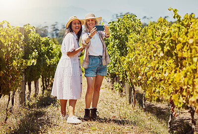 Full length of two happy friends taking selfies on a cellphone in a vineyard. Smiling women standing together and bonding during a day on a wine farm and taking pictures for social media with a phone