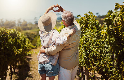 Buy stock photo Rearview of unknown senior couple making heart shape sign and symbol hand gesture and hugging on farm. Caucasian farmers standing together, bonding and embracing on vineyard. Elderly husband and wife