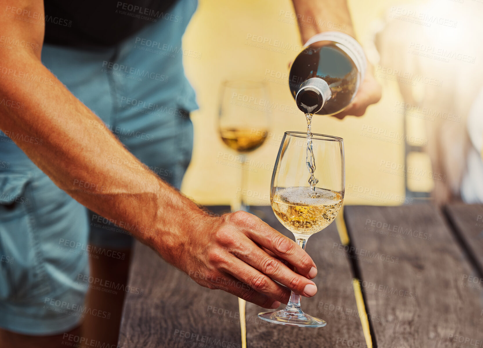 Buy stock photo Closeup of unknown farmer pouring white wine into wineglass on farm. Caucasian man holding a bottle and filling a glass with alcohol for tasting during summer on his vineyard. Weekend wine tasting