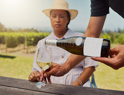 Unknown farmer pouring white wine into wineglass on farm for mixed race friend. Caucasian man holding bottle and filling glass with alcohol for tasting during summer on vineyard. Weekend wine tasting
