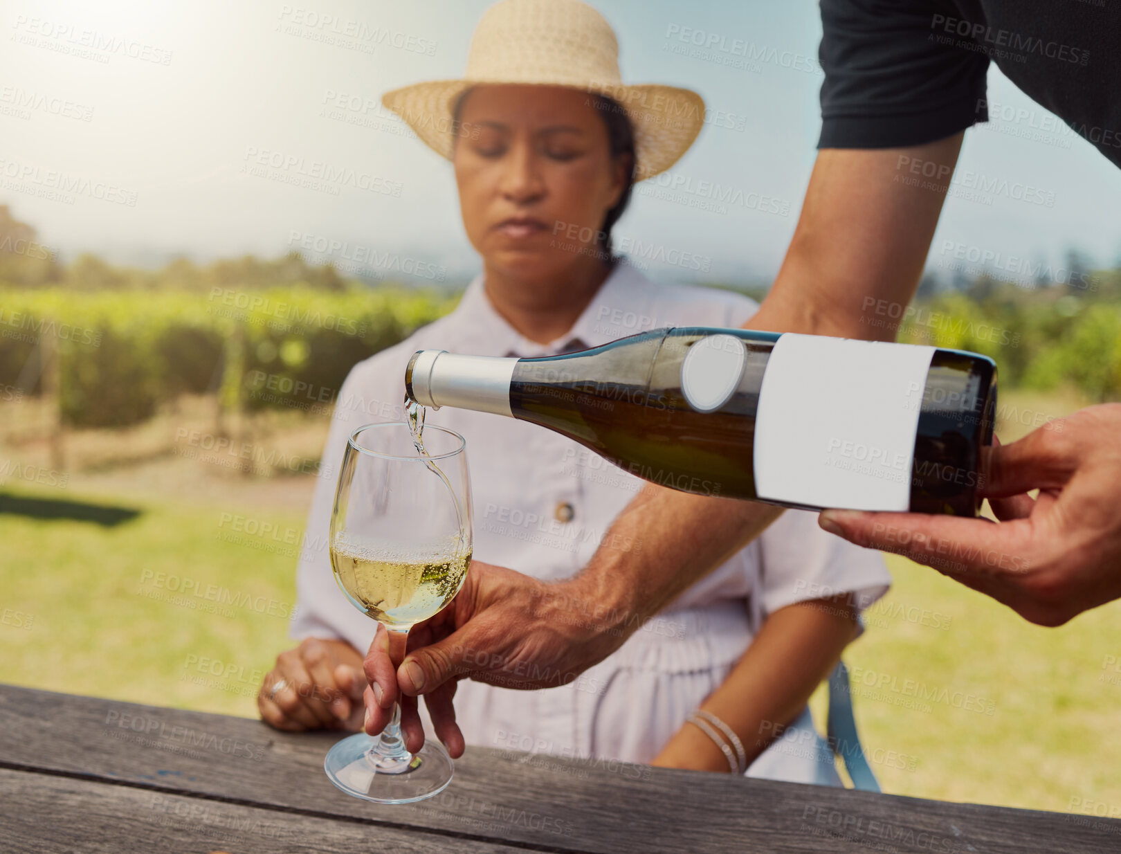 Buy stock photo Unknown farmer pouring white wine into wineglass on farm for mixed race friend. Caucasian man holding bottle and filling glass with alcohol for tasting during summer on vineyard. Weekend wine tasting
