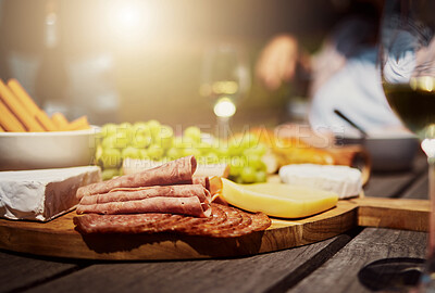 Closeup of a variety of snacks on a tapas wooden board outside on a table. Cheese, bread, fresh grapes and cold meats arranged for lunch on a vineyard. Food and wine tasting on a farm during a weekend