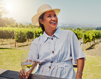 One smiling mature mixed race woman enjoying a wine tasting day on a farm. Happy hispanic woman wearing a hat while sitting alone on a vineyard. Woman holding a glass of white wine during the weekend
