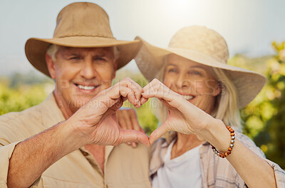 Portrait of smiling senior couple making heart shape sign and symbol hand gesture and hugging on farm. Caucasian farmers standing together, bonding and embracing on vineyard. Elderly husband and wife