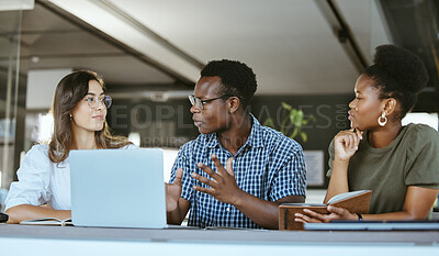 Buy stock photo Three young happy businesspeople having a meeting while sitting at a table and working on a laptop at work. Business professionals talking and planning in an office together. African american businessman talking to colleagues