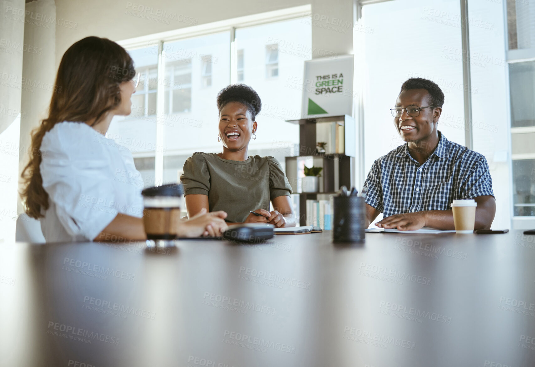Buy stock photo Three young happy businesspeople having a meeting while sitting at a table at work. Cheerful business professionals talking and planning in an office together