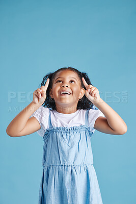 Excited little hispanic girl kid looking amazed and surprised while pointing her fingers up at copy space against blue studio background. Advertising childrens products