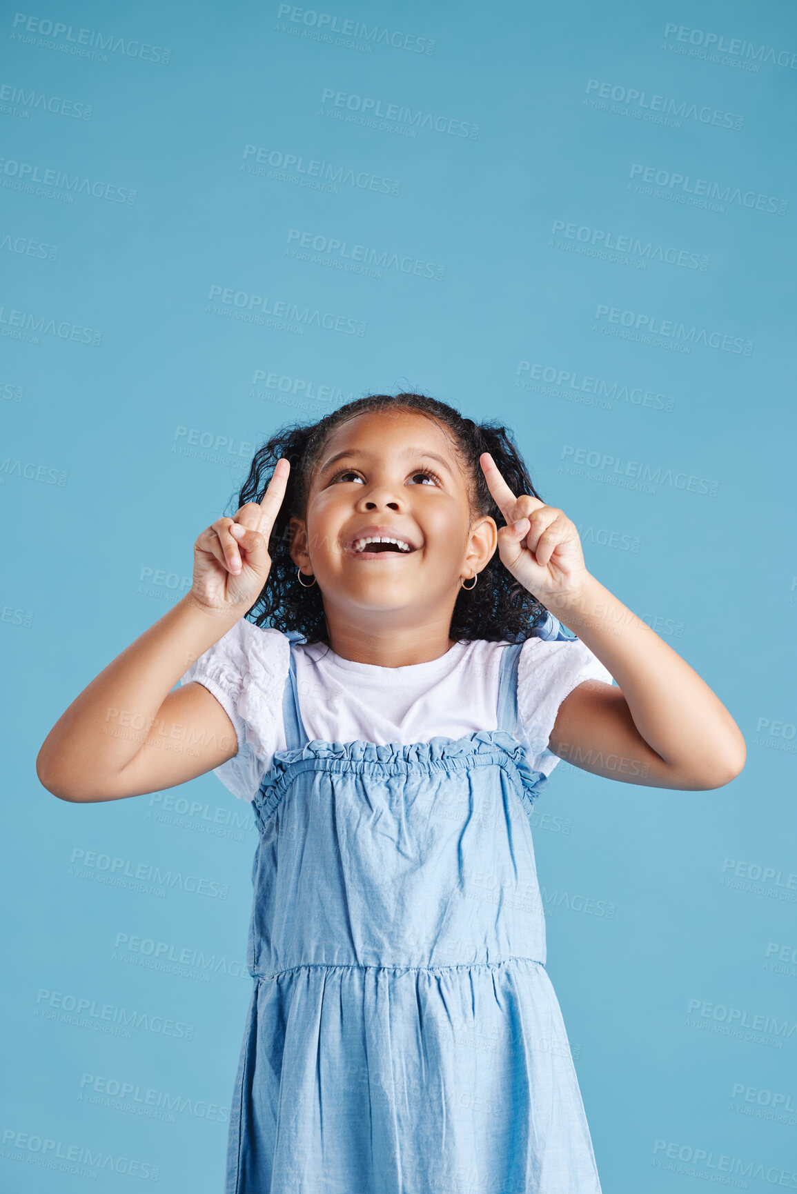 Buy stock photo Excited little hispanic girl kid looking amazed and surprised while pointing her fingers up at copy space against blue studio background. Advertising childrens products