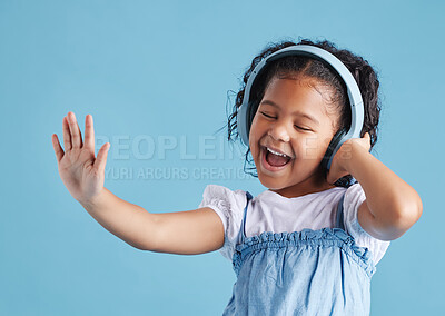 Buy stock photo Adorable little hispanic girl standing with her eyes closed and looking happy while listening to music with wireless headphones, dancing and singing along to her favourite song against a blue studio background