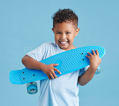Buy stock photo Excited little hispanic boy holding his skateboard. Happy smiling kid hugging skateboard after getting it as a gift against blue studio background