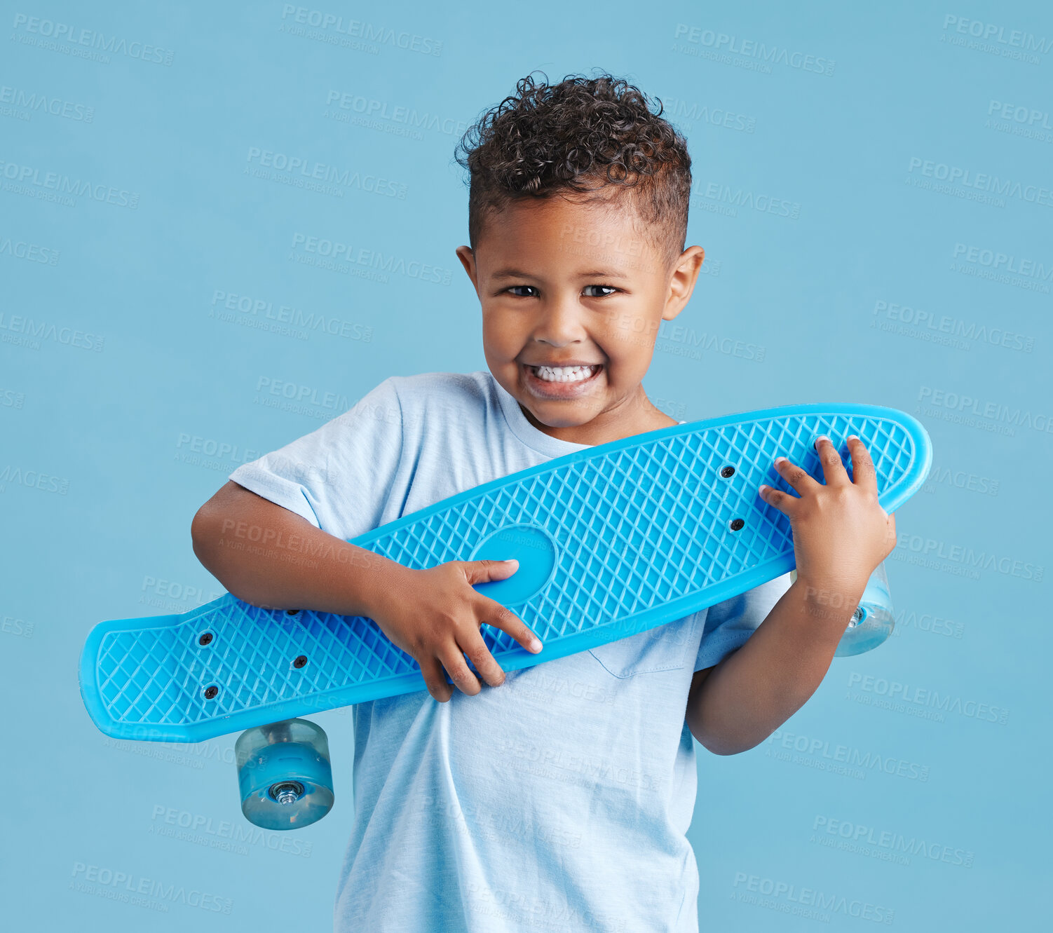 Buy stock photo Excited little hispanic boy holding his skateboard. Happy smiling kid hugging skateboard after getting it as a gift against blue studio background