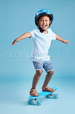 Buy stock photo Adorable little hispanic boy wearing his helmet for safety while riding his skateboard against a blue studio background