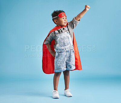 Brave cheerful boy in superhero cape and mask clenching his fist pretending to fly on blue background. Strong kid ready to save the world with his superpowers