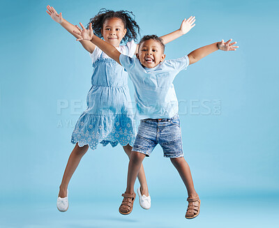Buy stock photo Full length portrait of cute girl and boy jumping with their arms outstretched and having fun on blue studio background. Happy little brother and sister siblings smiling and playing together