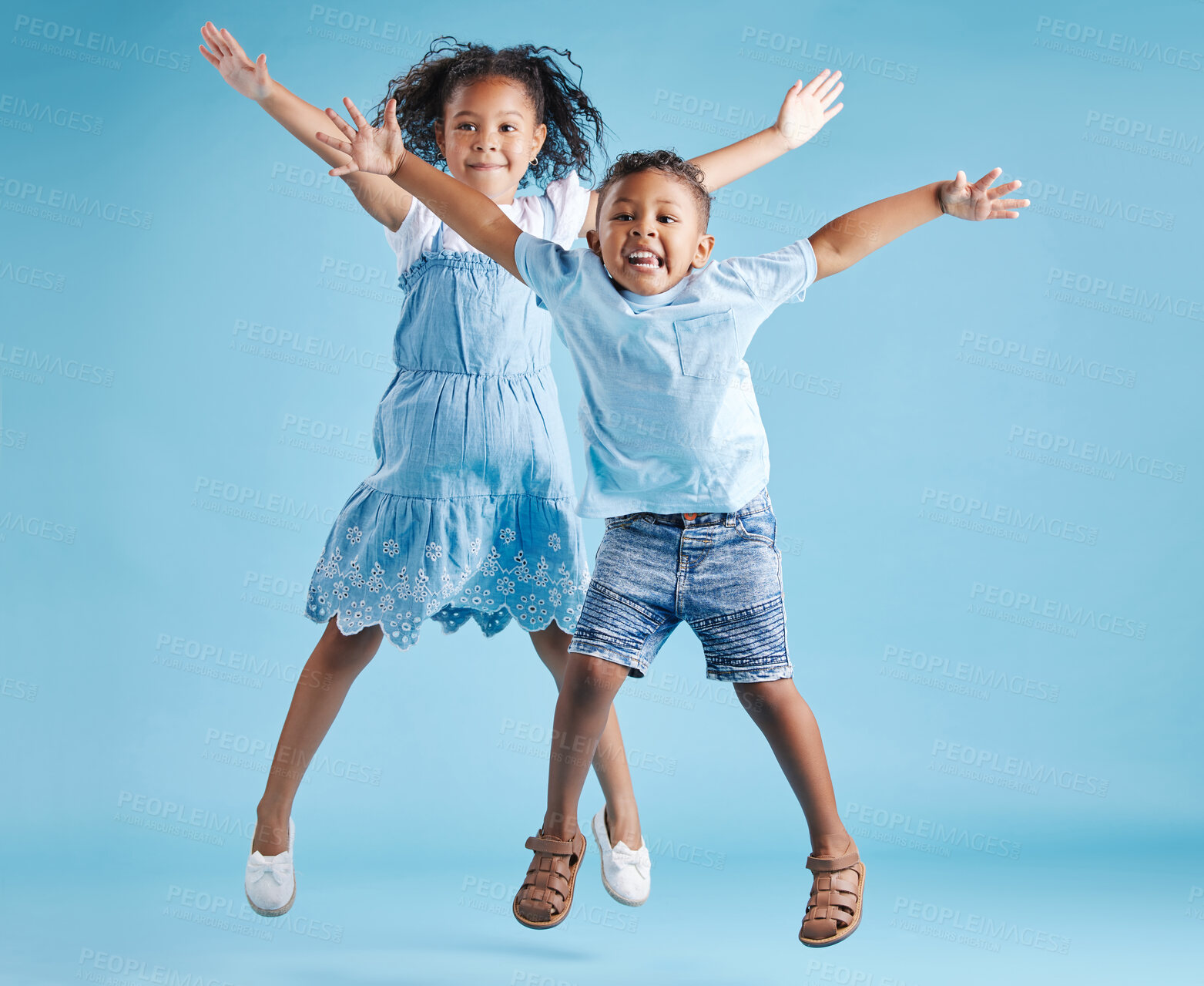 Buy stock photo Full length portrait of cute girl and boy jumping with their arms outstretched and having fun on blue studio background. Happy little brother and sister siblings smiling and playing together