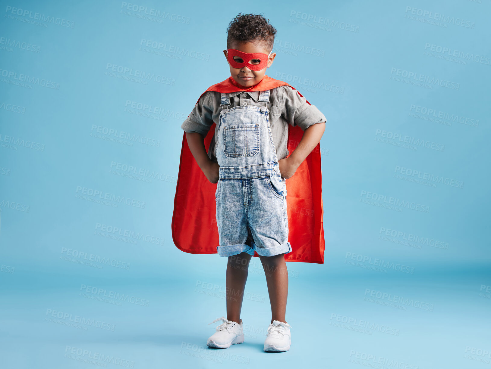 Buy stock photo Full length portrait of a brave little boy in superhero cape and mask standing with his hands on hips on blue background. Strong kid ready to save the world with his superpowers