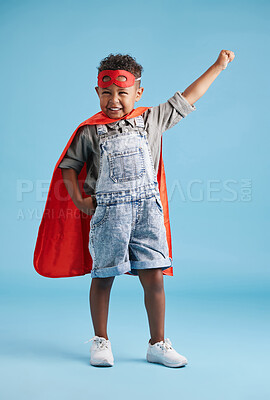 Portrait of cheerful little boy in superhero cape and mask stretching out his hand on blue background. Strong brave kid ready to save the world with his superpowers