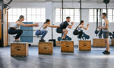 Diverse group of active young people doing box jump exercises together with a trainer in a gym. Focused athletes landing in a squat while doing bodyweight training during a workout in a fitness class