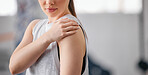 Closeup of one caucasian woman holding her sore shoulder while exercising in a gym. Female athlete suffering with painful arm injury from fractured joint and inflamed muscles during workout. Struggling with stiff body cramps causing discomfort and strain