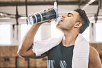 Young athlete drinking water after a workout. Fit man taking a break to hydrate. Always have a water bottle when exercising at the gym. Bodybuilder drinking from a water bottle in the gym