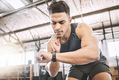 Buy stock photo Fit trainer checking his pulse after a workout. Young athlete timing his progress on a watch after exercise. Bodybuilder tracking his heartbeat during a training exercise. Sporty man in the gym