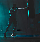 Silhouette of an unrecognizable boxer man sparring with a punching bag in a dark gym. Male athlete working out in preparation for his upcoming fight. Young martial artist training and practicing