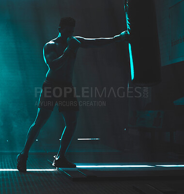 Silhouette of an unrecognizable boxer man sparring with a punching bag in a dark gym. Male athlete working out in preparation for his upcoming fight. Young martial artist training and practicing