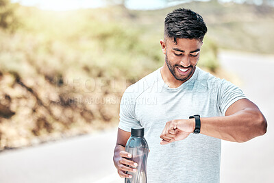 Buy stock photo Athletic young mixed race man looking at his watch while exercising outdoors. Handsome hispanic male holding a water bottle and checking the time during a workout. Tracking progress while working out