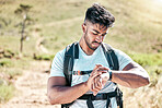 Athletic young mixed race man looking at his watch while hiking outdoors. Handsome hispanic resting while checking the time on his smartwatch during a workout. Tracking progress while taking a hike
