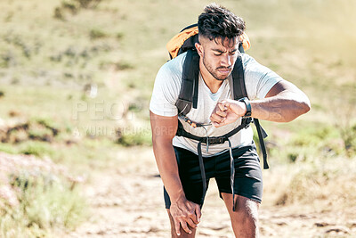 Buy stock photo Athletic young mixed race man looking at his watch while hiking outdoors. Handsome hispanic resting while checking the time on his smartwatch during a workout. Tracking progress while taking a hike
