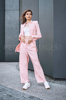 A young trendy and confident mixed race woman looking stylish while posing and spending time in the city. Fashionable hispanic woman wearing pink clothes chilling downtown wearing matching sneakers