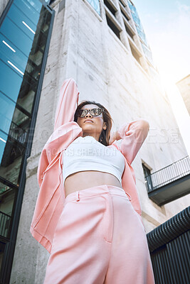 A young trendy and confident mixed race woman looking stylish while posing and spending time in the city. Fashionable hispanic woman wearing pink clothes and sunglasses