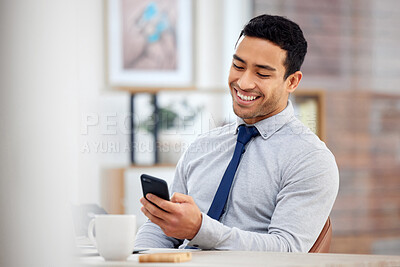 Young happy mixed race businessman holding and using a phone sitting in an office at work. One hispanic male businessperson smiling while using social media on a cellphone sitting at a desk