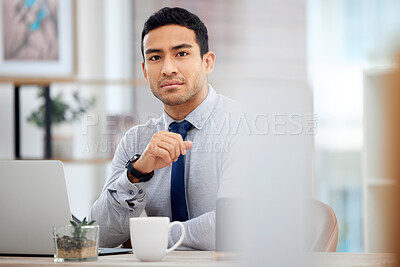 Buy stock photo Young serious mixed race businessman working on a laptop alone in an office at work. One focused hispanic businessperson sitting at a desk at work
