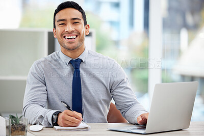 Portrait of a cheerful mixed race businessman writing in a diary while working on a laptop alone in an office at work. One content hispanic male businessperson taking notes in a book while sitting at a desk at work