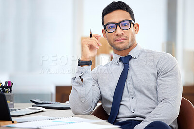 Buy stock photo Young mixed race businessman going through a report alone in an office at work. One focused hispanic male businessperson sitting at a desk in an office
