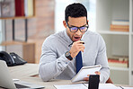 Young tired mixed race businessman reading notes In a notebook alone in an office at work. One hispanic male businessperson yawning while writing in a diary sitting at a desk in an office